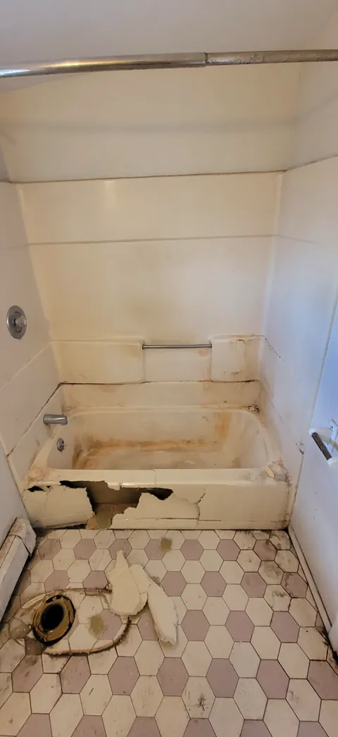 Old bathroom with a cracked tub surround and worn hex floor tile