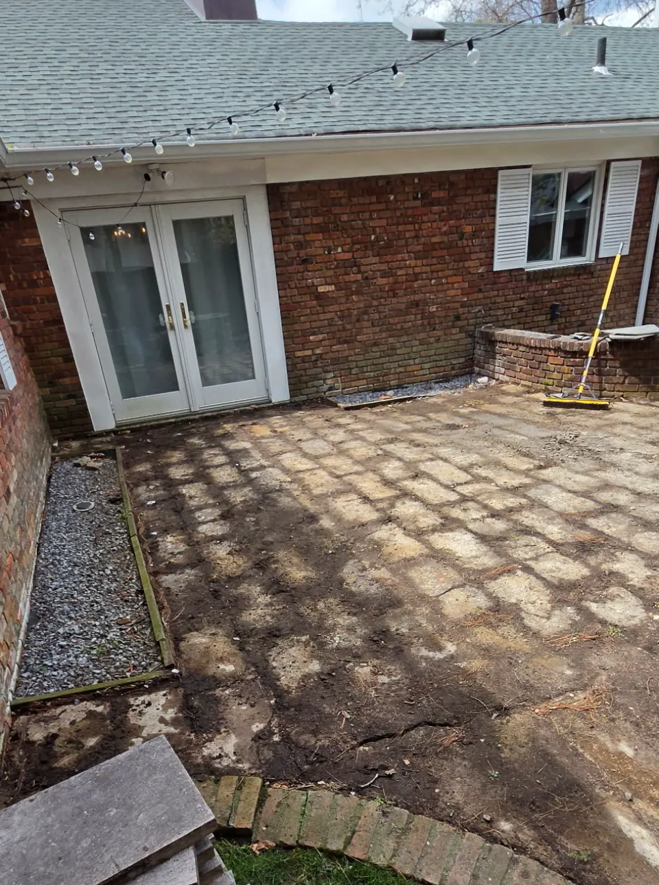 Old patio torn up to bare ground outside a pair of French doors